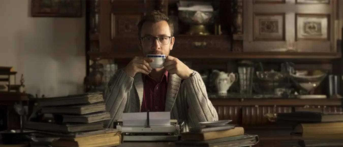 Ein Mann mittlerem Alters der sich eine Tasse mit schwarzem Kaffee zum Mund führt und in die Kamera blickt.