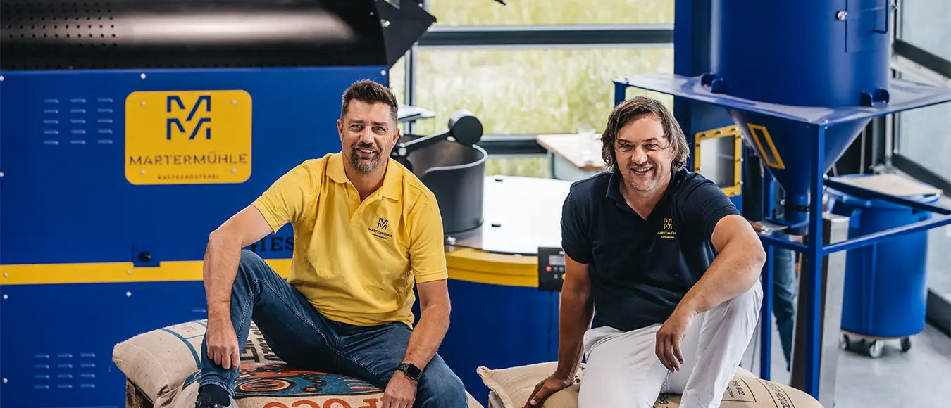 Peter Vit und Ralf Heincke, Gründer der Kaffeerösterei Martermühle auf Kaffeesäcken sitzend vor einem Trommelröster