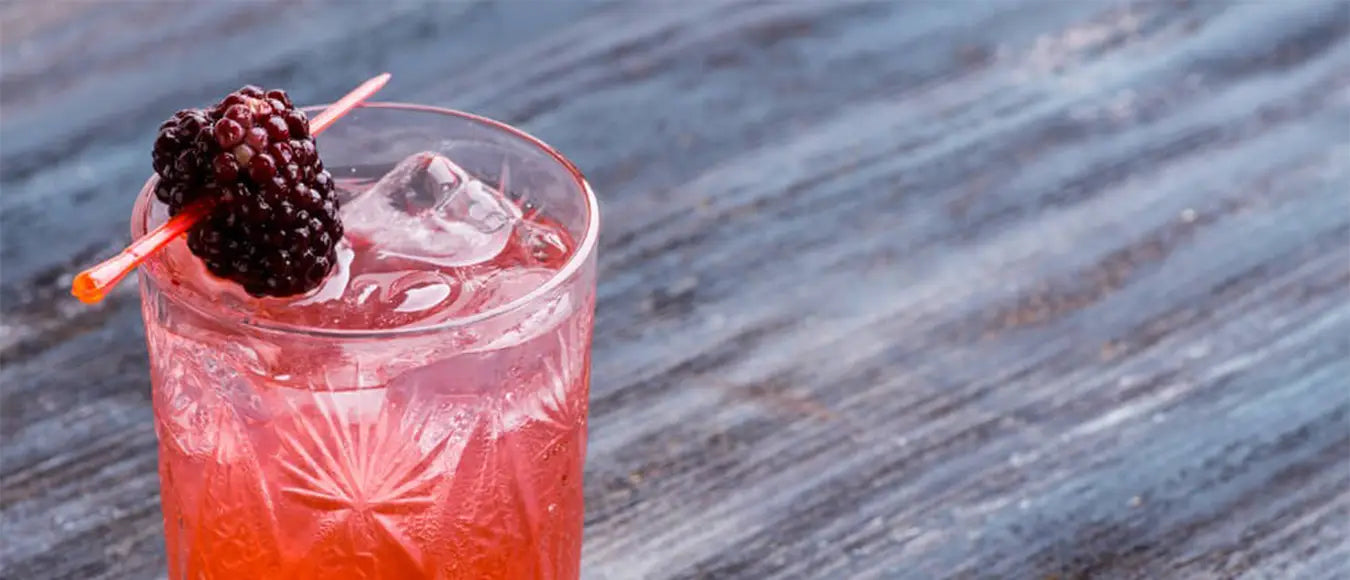 Ein Glas mit roter Flüssigkeit, Eiswürfeln und einer Himbeere am Spieß