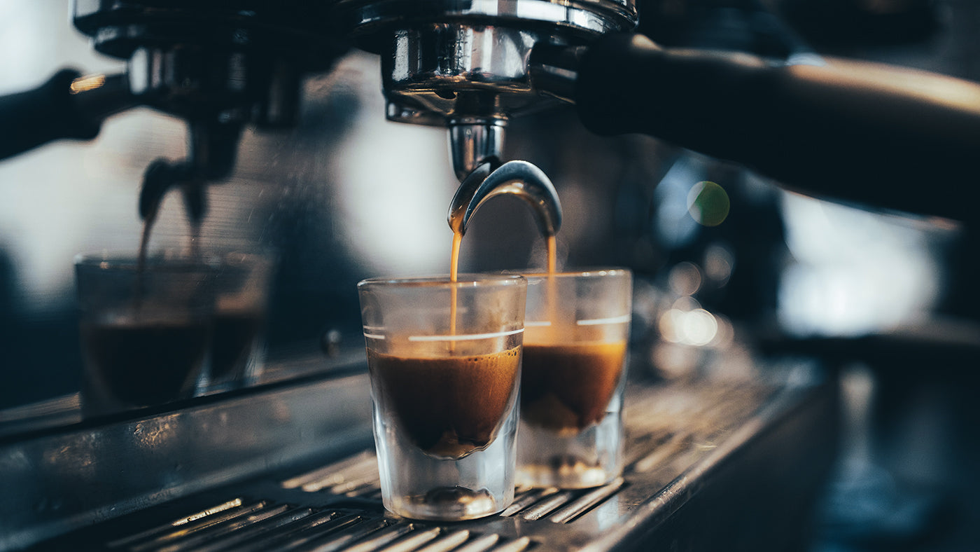 Frischer Espresso fließt aus einem doppelten Siebträger einer Siebträgermaschine in zwei transparente Shotgläser