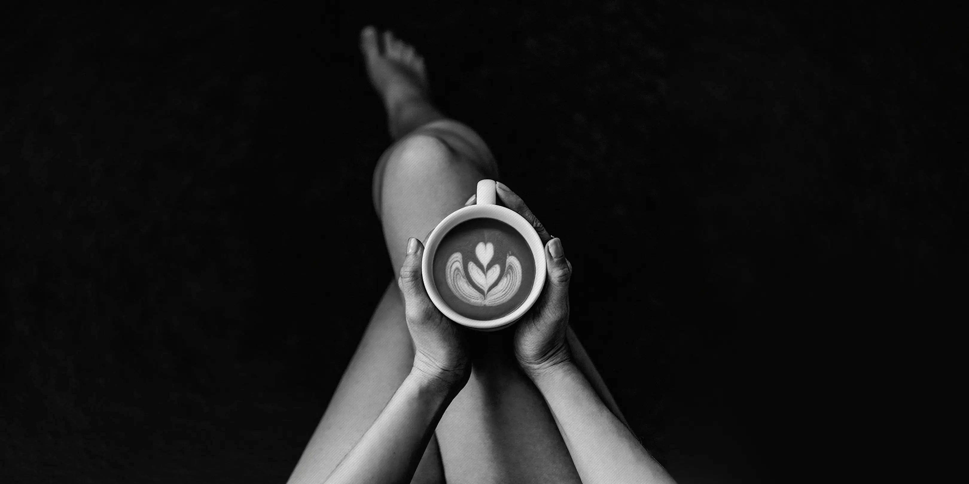 Überschlagene Frauenbeine mit einer Cappuccinotasse mit Latte Art in der Hand.