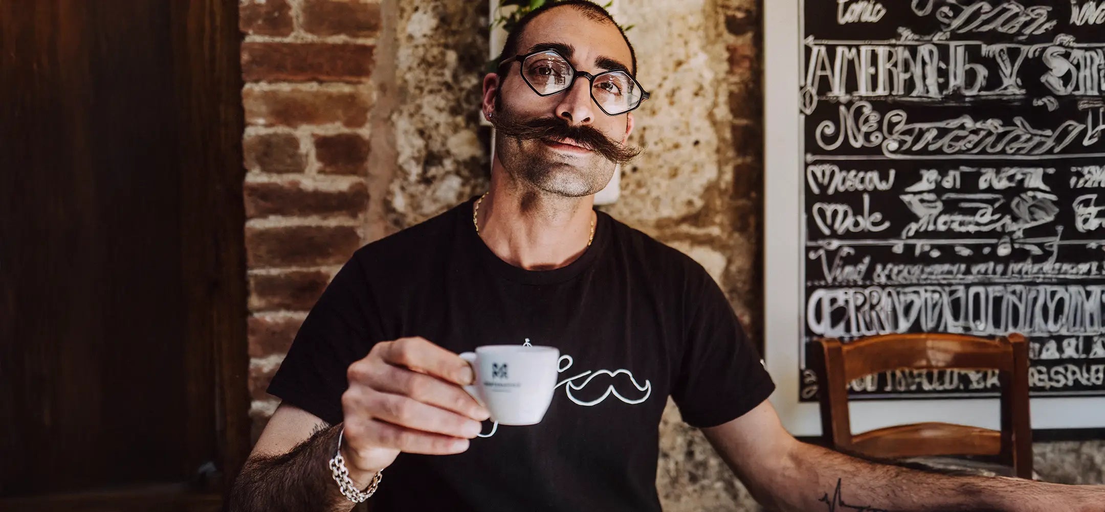 Italiener Pepe mit eckiger Brille, aufgezwirbelten Schnurrbart und einer Martermühle-Espressotasse in der Hand.