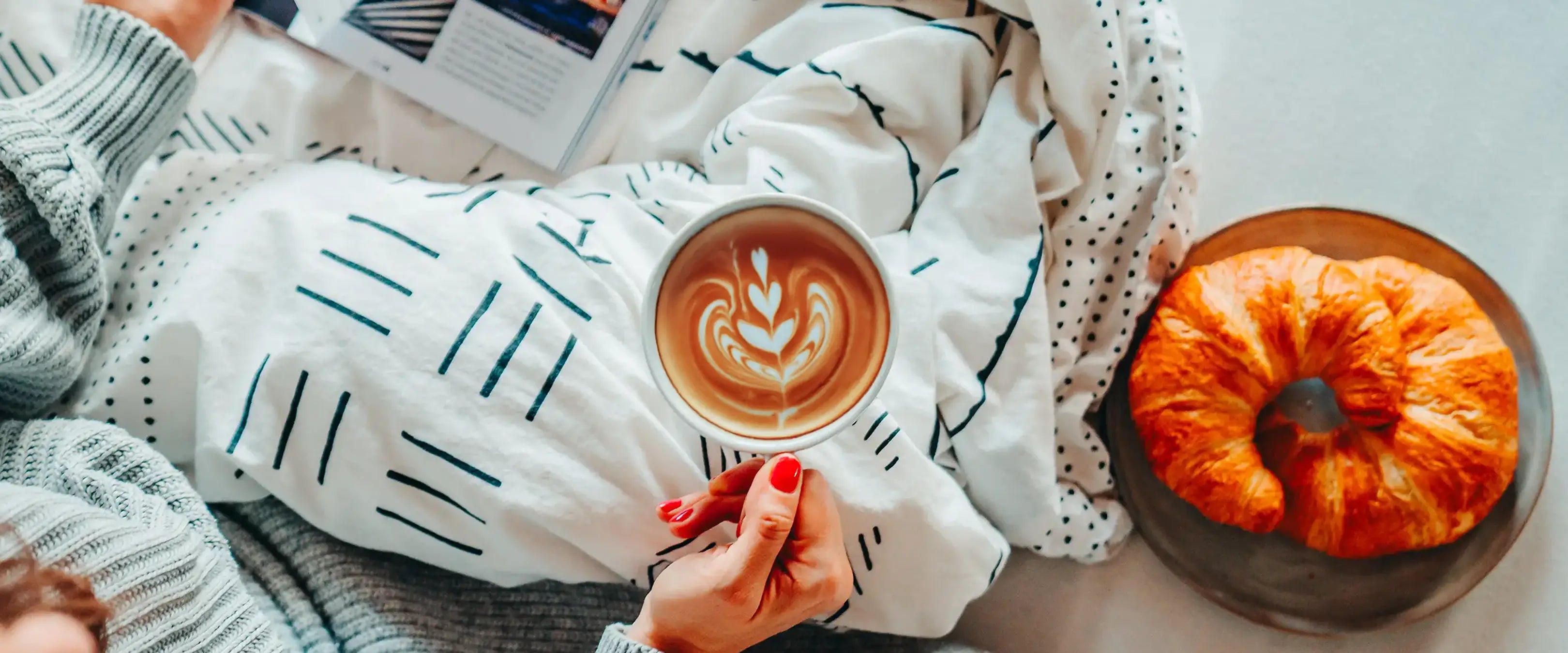 Entkoffeinierter Cappuccino im Bett mit zwei Croissants auf einem Teller.