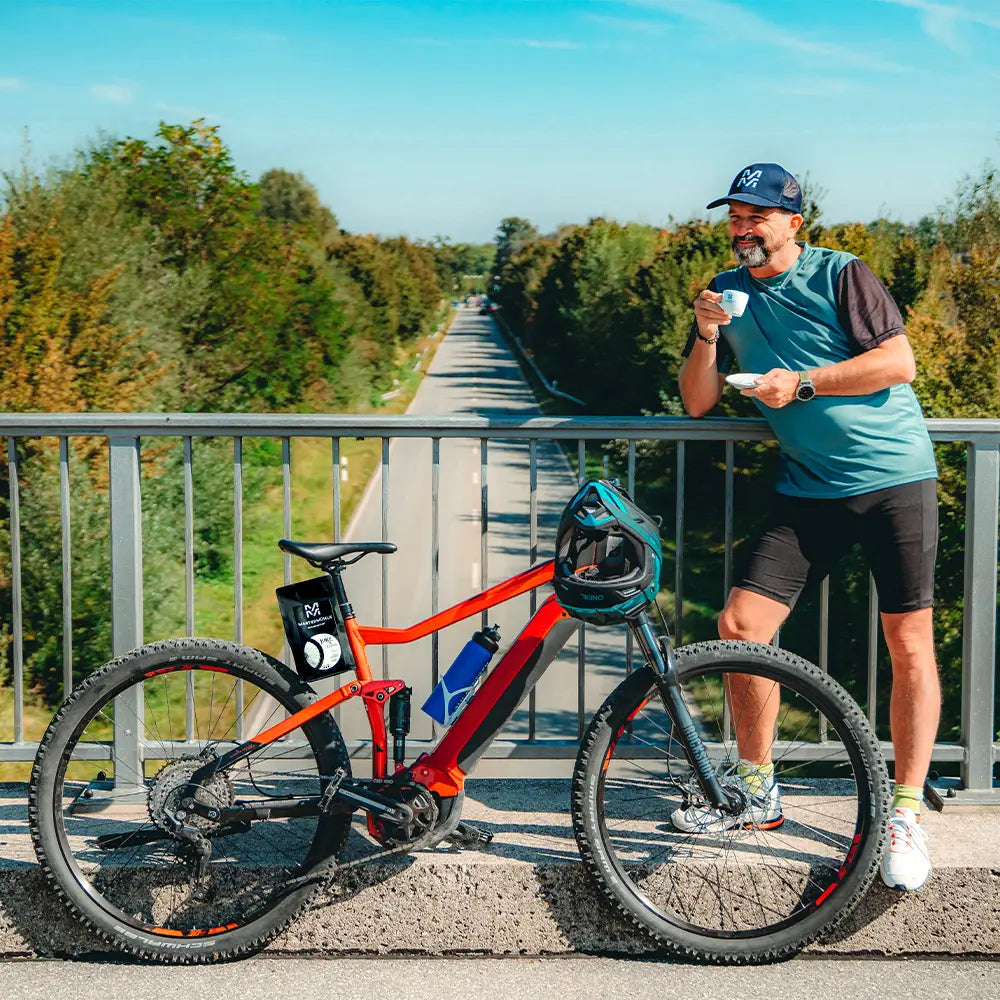 Mann mit seinem Fahrrad und dem Bike Espresso, der an einer Brücke steht und Espresso trinkt.