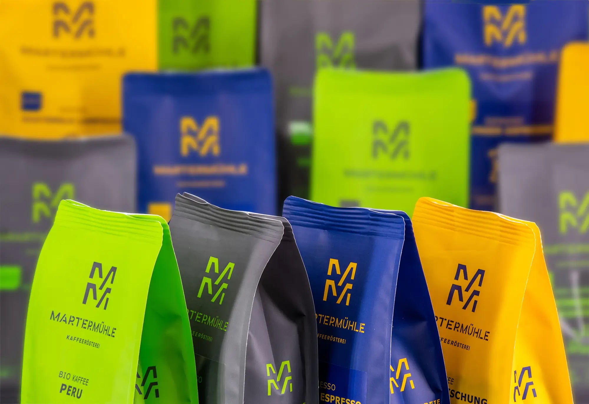 Vier Martermühle Kaffeepackungen in verschiedenen Farben mit ganz vielen bunten Packungen im Hintergrund.