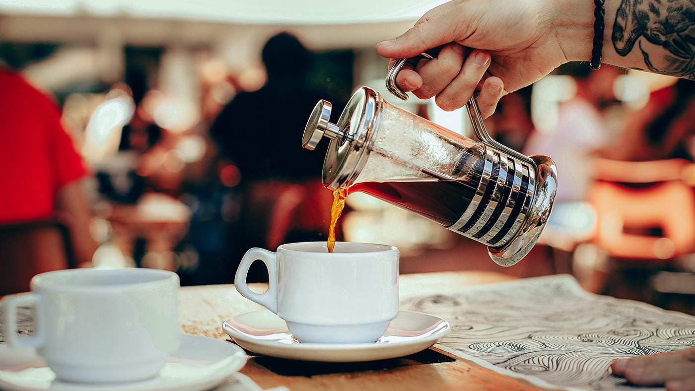 Eine Stempelkanne aus der ein Kaffee in eine Tasse eingefüllt wird.
