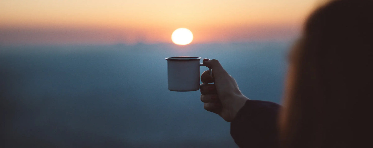 Eine Frau die eine Tasse der Kaffeerösterei Martermühle in Richtung Sonnenuntergang hält