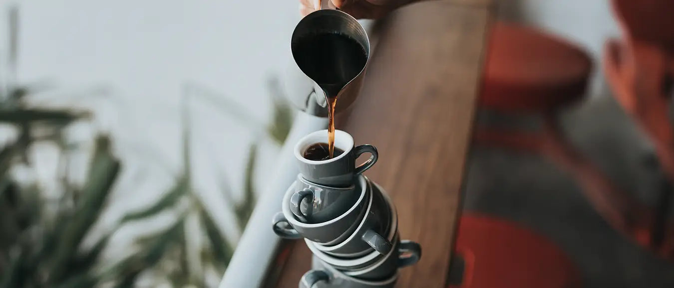 Ein Stapel aus Espressotassen der Kaffeerösterei Martermühle, in die oberste wird frischer Espresso gefüllt