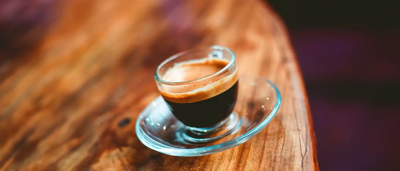 Eine kunstvolle transparente Espressotasse auf einem Holztisch der Kaffeerösterei Martermühle mit frischem Espresso