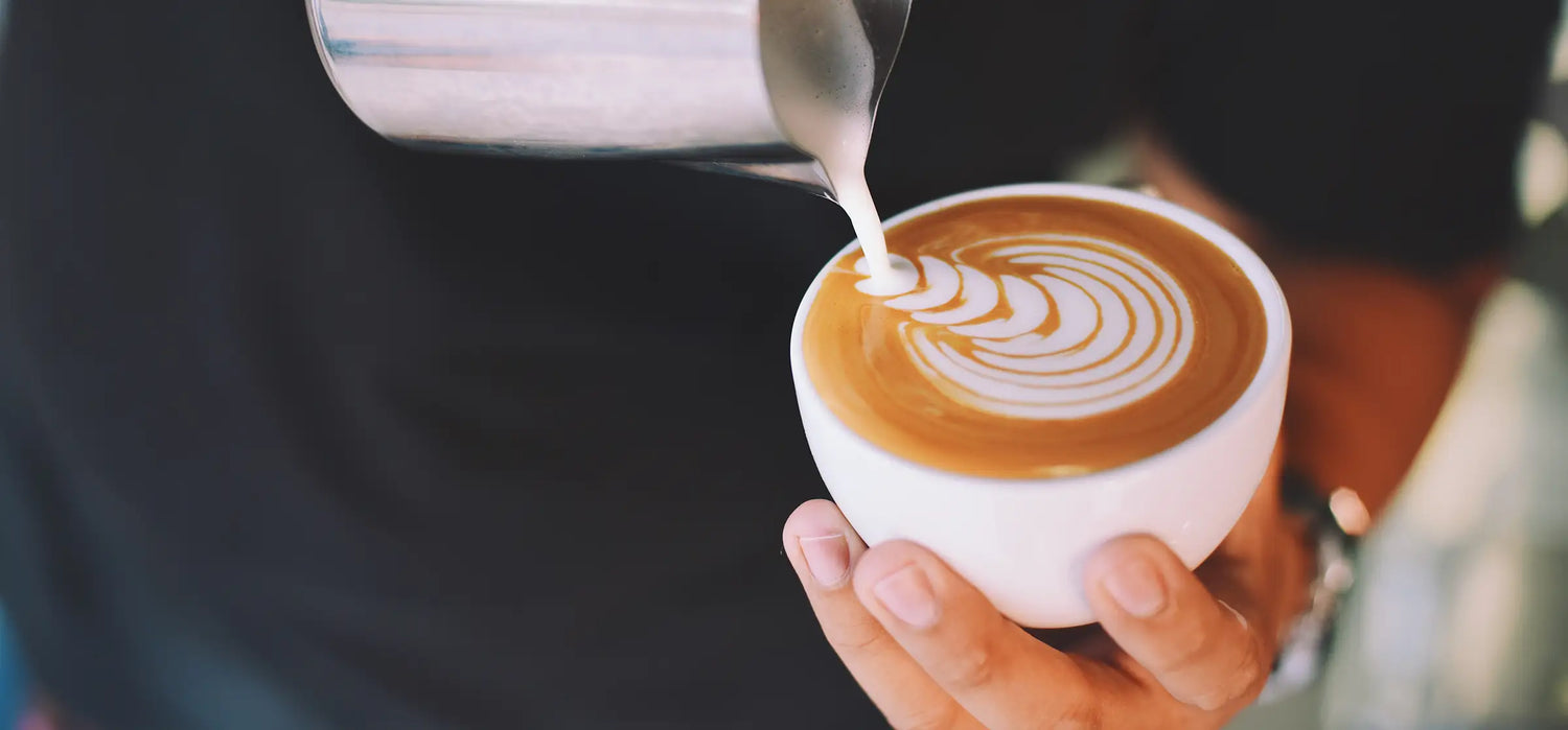 Milch wird in einen Cappuccino der Kaffeerösterei Martermühle gegossen um ein Muster auf den Kaffee zu zeichnen