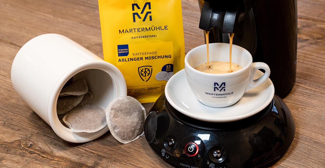 Eine Packung Kaffeepads der Kaffeerösterei Martermühle und eine Pad Maschine die frischen Kaffee zubereitet.
