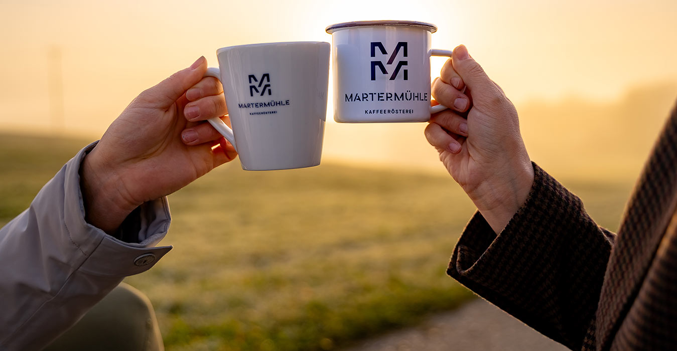 Zwei Frauen stoßen im Sonnenuntergang mit zwei Tassen der Kaffeerösterei Martermühle an.