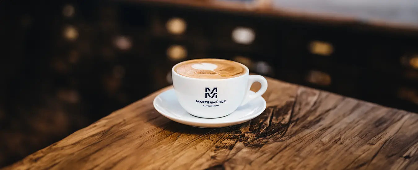 Nahaufnahme einer Cappuccino Tasse der Kaffeerösterei Martermühle auf einem rustikalen Holztisch