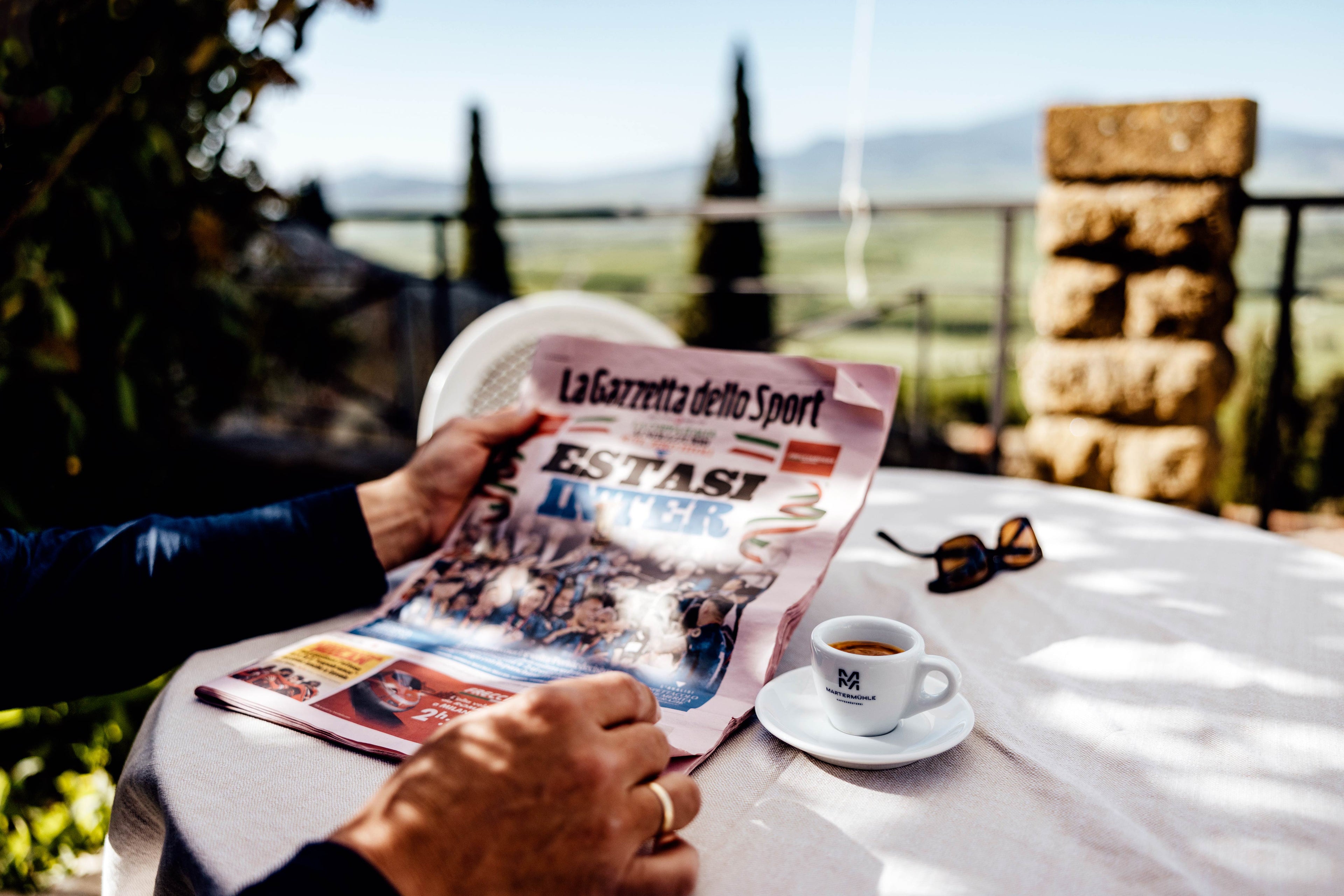 Eine Nahaufnahme eines Lesers der La Gazzetta auf einer italienischen Terrasse mit einer Espressotasse der Kaffeerösterei Martermühle