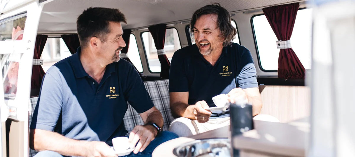 Peter Vit und Ralf Heincke in einem alten Camper Bus lachen und trinken Espresso der Kaffeerösterei Martermühle