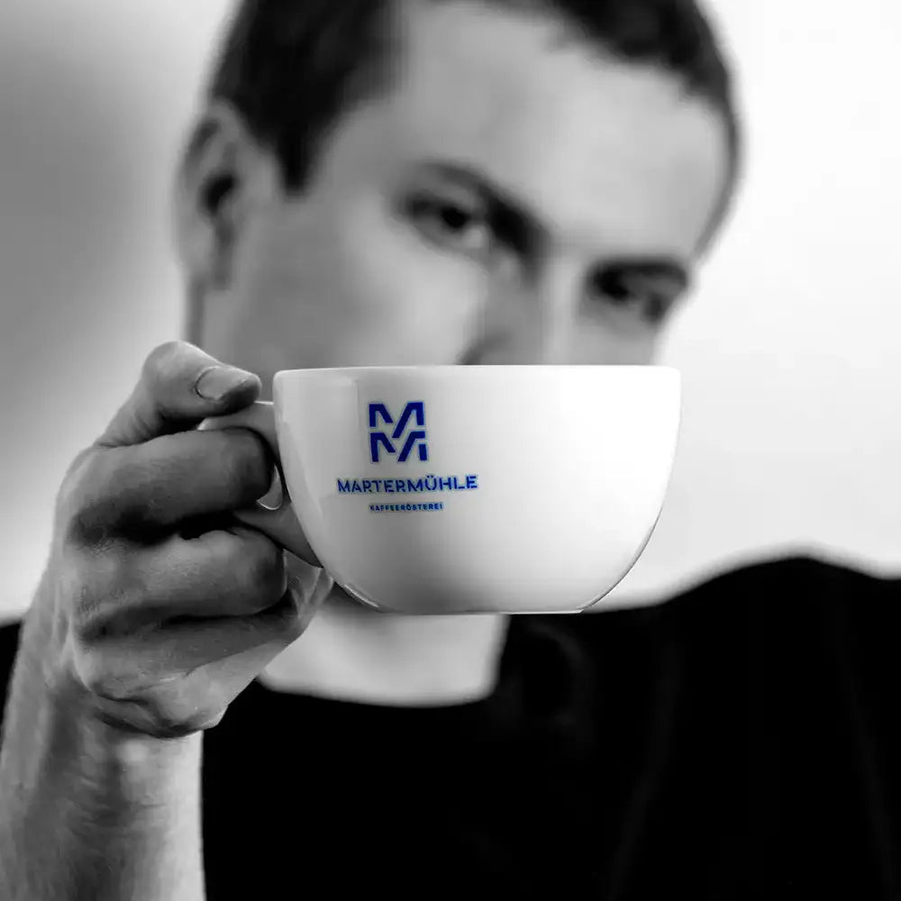 Ein Junger Mann hält eine Martermühle Kaffeerösterei Cappuccino Tasse in die Kamera